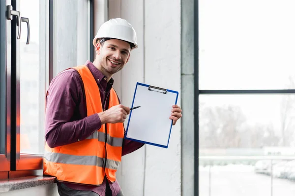 Cheerful fireman in helmet and uniform holding clipboard with blank paper — Stock Photo