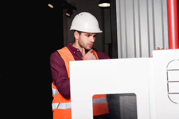 Pensive fireman in helmet standing and looking at fire panel — Stock Photo