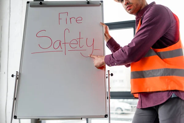 Cropped view of fireman pointing with finger while standing near white board with fire safety lettering — Stock Photo