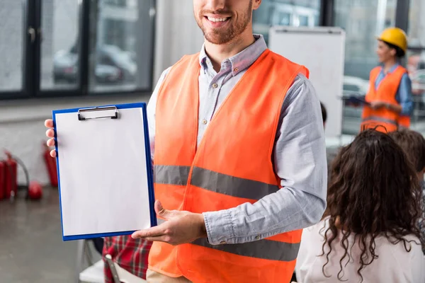 Abgeschnittene Ansicht eines lächelnden Feuerwehrmannes mit leerem Klemmbrett in der Nähe eines Mitarbeiters, der einen Vortrag über das Briefing hält — Stockfoto