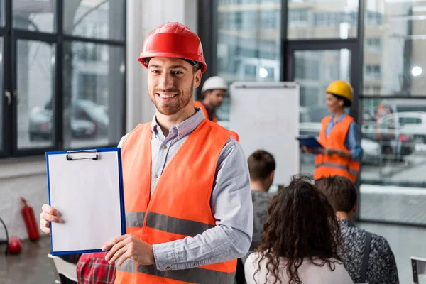 Cheerful fireman holding blank clipboard near coworkers giving talk on briefing — Stock Photo