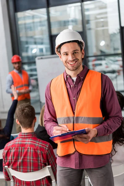 Selektiver Fokus eines gut gelaunten Feuerwehrmannes mit Klemmbrett in der Nähe eines Mitarbeiters, der einen Vortrag über Einweisung hält — Stockfoto