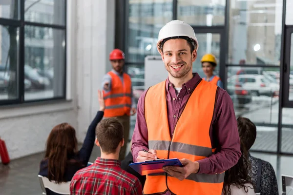 Selective focus of happy fireman holding clipboard near coworker giving talk on briefing — Stock Photo