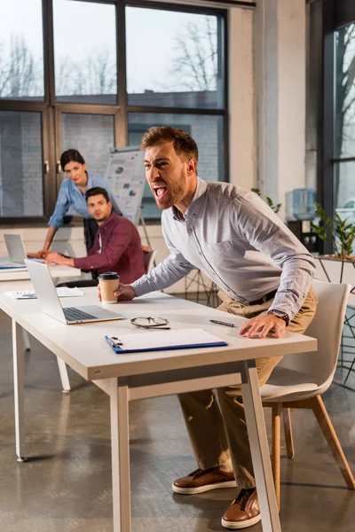 Terrified businessman holding paper cup and screaming near coworkers in office — Stock Photo