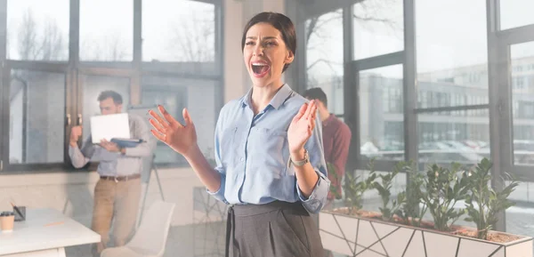 Scared businesswoman screaming while standing near coworkers in office with smoke — Stock Photo