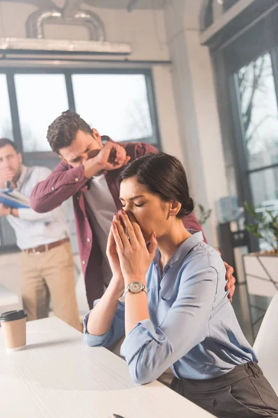 Businesswoman sitting with closed eyes and holding nose near coworkers in office with smoke — Stock Photo