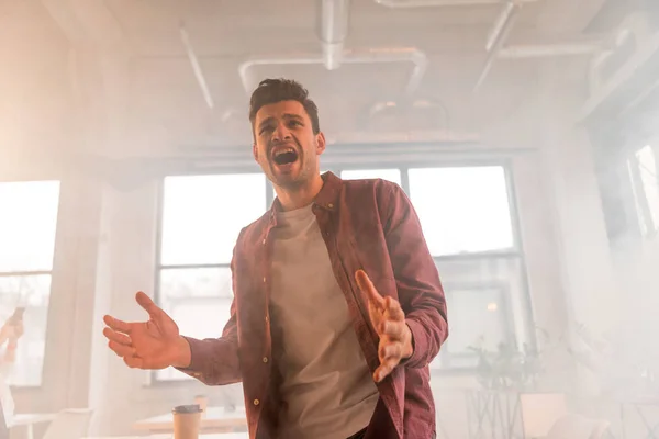 Gutaussehender Geschäftsmann brüllt im Büro mit Rauch — Stockfoto