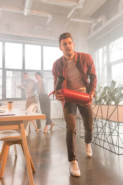 Scared businessman holding extinguisher in office with smoke near coworkers — Stock Photo