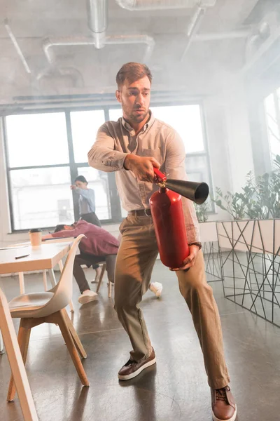 Frightened businessman holding extinguisher in office with smoke near colleagues — Stock Photo
