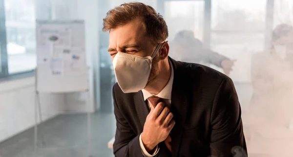 Enfoque selectivo de empresario asustado de pie en la máscara en la oficina con humo cerca de compañeros de trabajo — Stock Photo