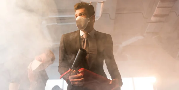 Hombre de negocios asustado en la máscara de retención de extintor cerca de compañero de trabajo en la oficina con humo — Stock Photo