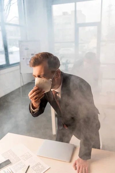 Uomo d'affari in maschera in piedi vicino alla scrivania con collega in ufficio con fumo — Foto stock