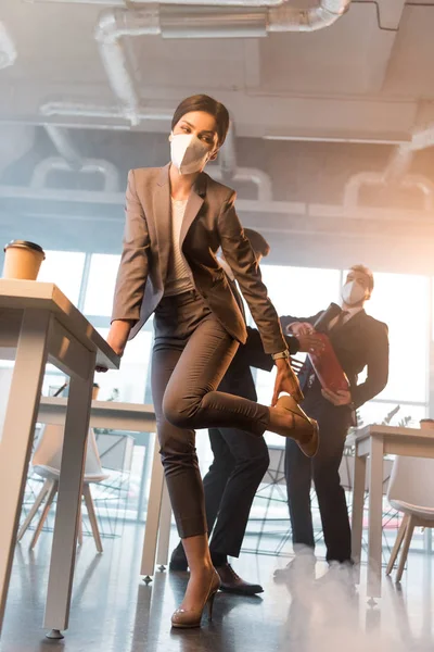 Businesswoman in mask holding shoe while standing near coworkers in office with smoke — Stock Photo