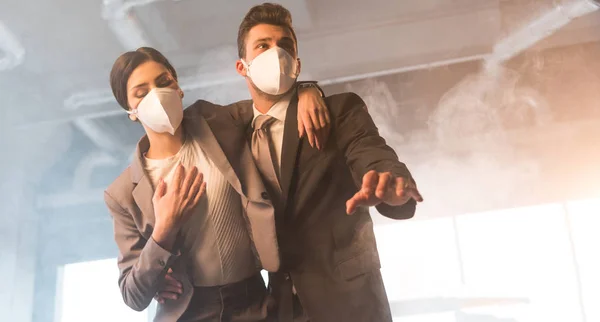 Scared businessman in mask standing with female coworker in office with smoke — Stock Photo