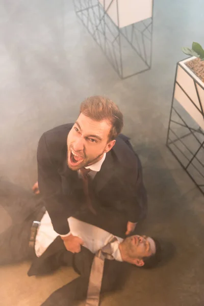 Overhead view of businessman screaming near colleague lying on floor in office with smoke — Stock Photo