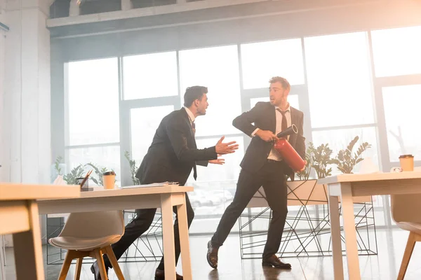 Scared businessman talking with coworker holding extinguisher while walking in office with smoke — Stock Photo