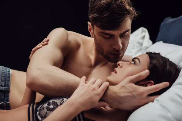 Bonito homem gentilmente abraçando bela mulher na cama isolado no preto — Fotografia de Stock