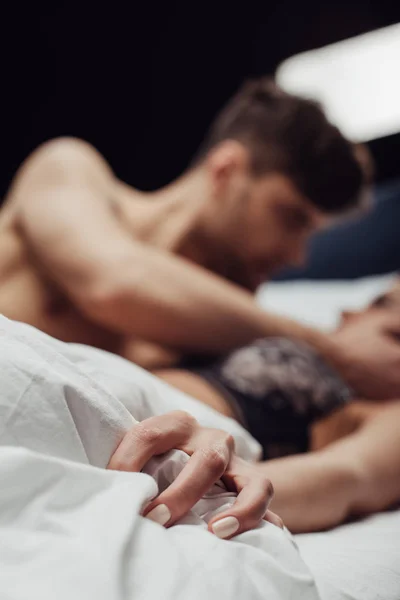 Selective focus of woman holding blanket while lying in bed with man isolated on black — Stock Photo