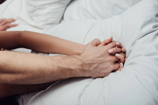 Vue recadrée du couple tenant la main et couché dans le lit à la maison — Stock Photo