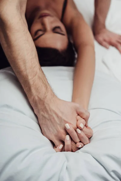Enfoque selectivo de pareja cogida de la mano y acostada en la cama en casa - foto de stock