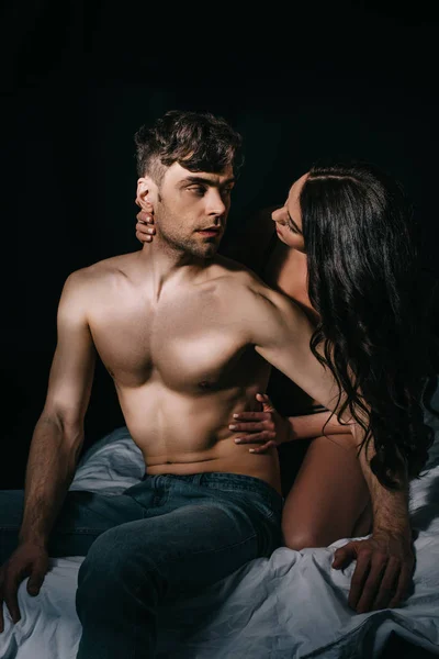 Femme embrassant bel homme torse nu au lit isolé sur noir — Photo de stock