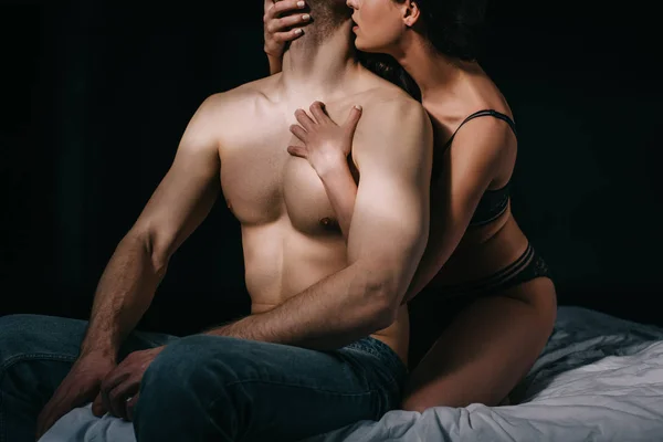 Обрезанный вид женщины, целующейся и обнимающей мускулистого мужчину в постели, изолированного на черном — стоковое фото