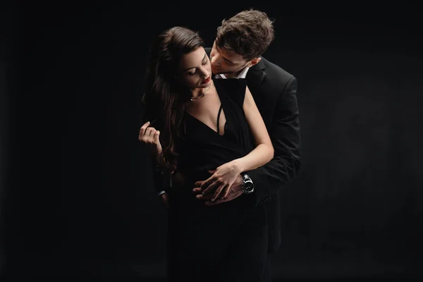 Пристрасна молода пара в офіційному одязі цілується ізольовано на чорному — стокове фото