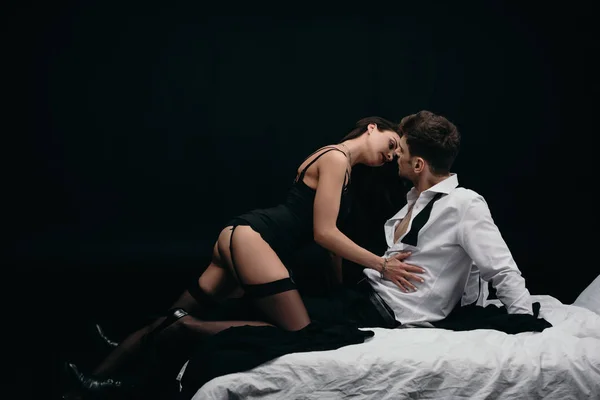 Sexy Frau in Strümpfen berührt leidenschaftlich Mann in formeller Kleidung isoliert auf schwarz mit Kopierraum — Stockfoto