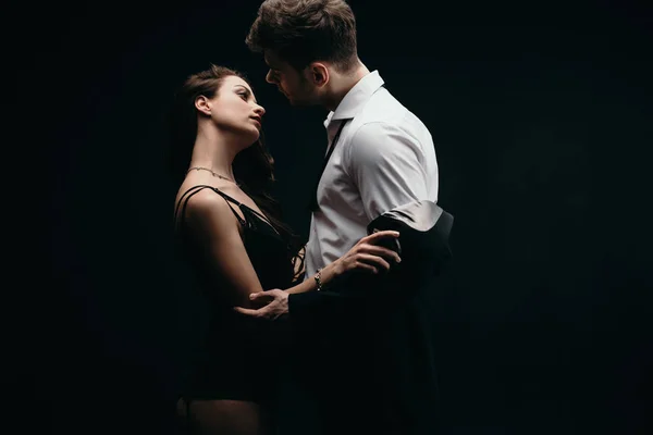 Beautiful sexy woman undressing man in formal wear isolated on black — Stock Photo