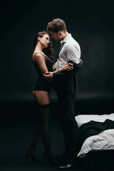 Bella donna sexy spogliarsi uomo in abito formale su sfondo nero — Foto stock