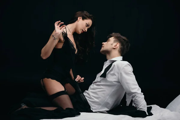 Bela jovem mulher no sexy lingerie despindo homem isolado no preto — Fotografia de Stock