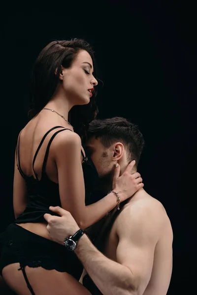 Hermosa mujer en ropa interior sexy sentado y tocando cuello de hombre aislado en negro — Stock Photo