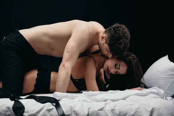 Young man kissing beautiful sexy woman in bed isolated on black — Stock Photo