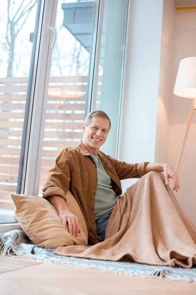Fröhlicher Mann sitzt im neuen Zuhause vor großem Fenster auf dem Boden — Stockfoto