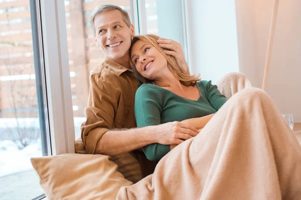 Happy couple embracing while sitting on floor by large window — Stock Photo
