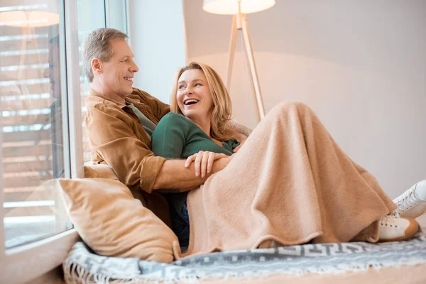 Sonriente pareja hablando mientras descansa en el suelo bajo la manta de lana - foto de stock