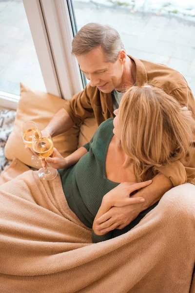 Happy couple hugging and clinking glasses of white wine while sitting on floor at new home — Stock Photo