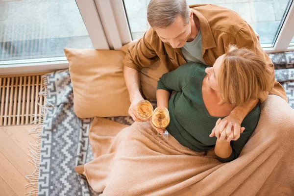 Vue aérienne du couple assis sur le sol par une grande fenêtre et des verres à vin blanc — Photo de stock