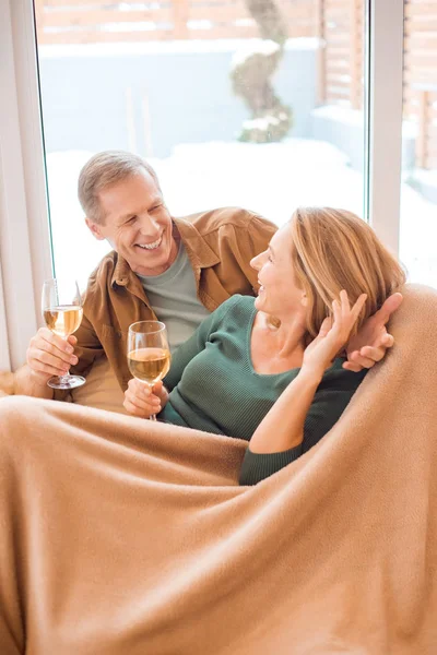 Happy couple holding glasses of white wine while resting under soft fleece blanket — Stock Photo