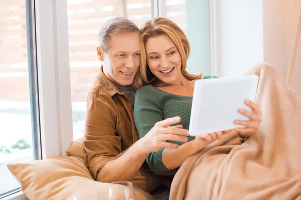 Smiling couple using digital tablet together while sitting by window — Stock Photo