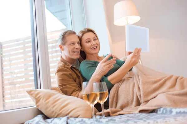 Happy couple using digital tablet while sitting of floor under soft fleece blanket — Stock Photo