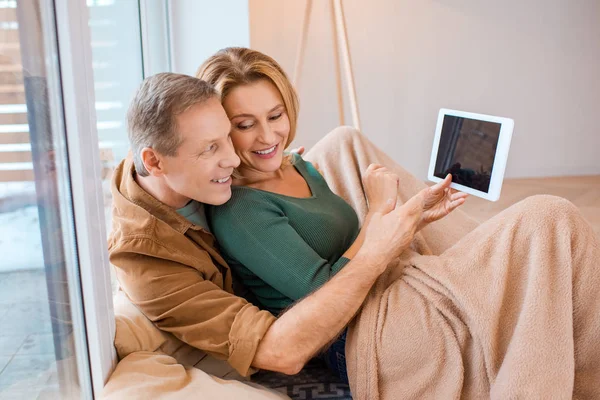 Happy couple using digital tablet while sitting under fleece blanket — Stock Photo