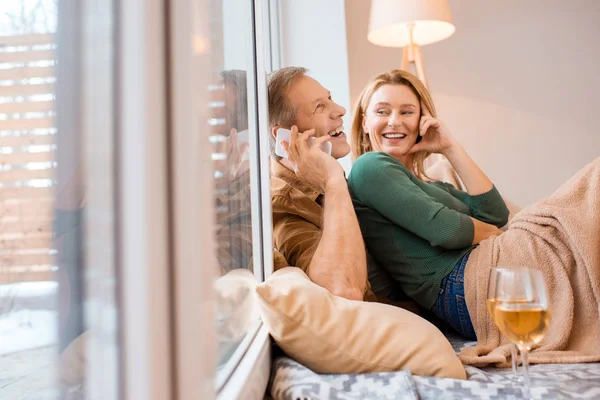 Hombre alegre hablando en el teléfono inteligente mientras está sentado en el suelo con la esposa - foto de stock