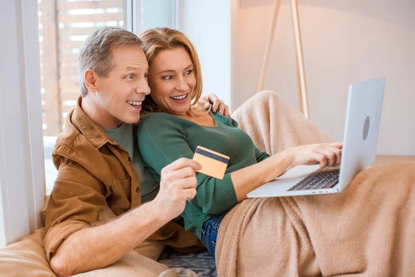 Casal animado usando laptop enquanto marido segurando cartão de crédito — Fotografia de Stock