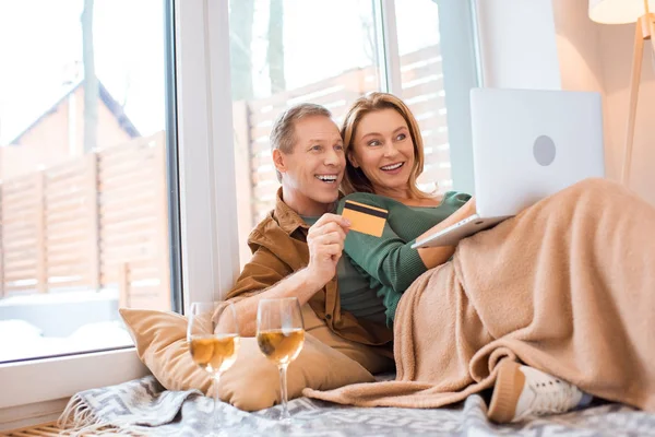 Alegre pareja usando portátil mientras marido celebración de tarjeta de crédito - foto de stock