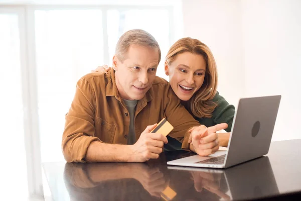 Усміхнена пара використовує ноутбук, а чоловік тримає кредитну картку — стокове фото