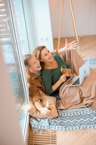 Взволнованная пара смотрит вверх, сидя на полу в новом доме и с помощью ноутбука — стоковое фото