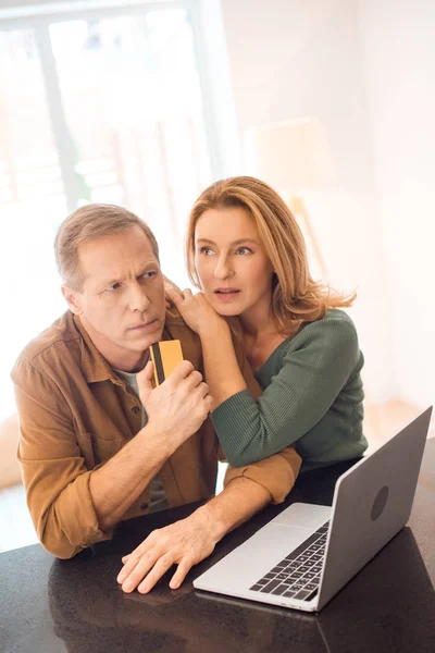 Casal pensativo em pé por laptop enquanto marido segurando cartão de crédito — Fotografia de Stock