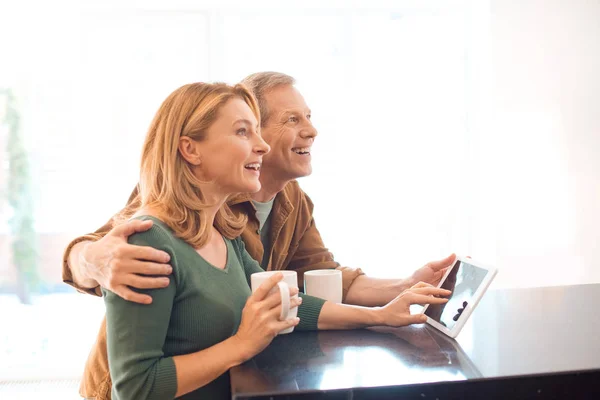 Glückliches Paar hält Kaffeetassen während es digitales Tablet benutzt — Stockfoto