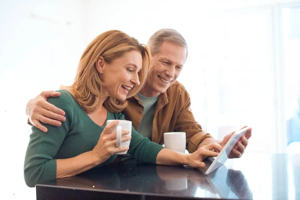 Casal feliz com xícaras de café usando tablet digital — Fotografia de Stock